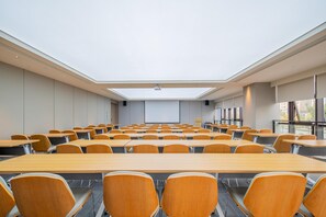 Sala de conferências com teto alto, claraboia e fileiras de mesas e cadeiras de madeira.