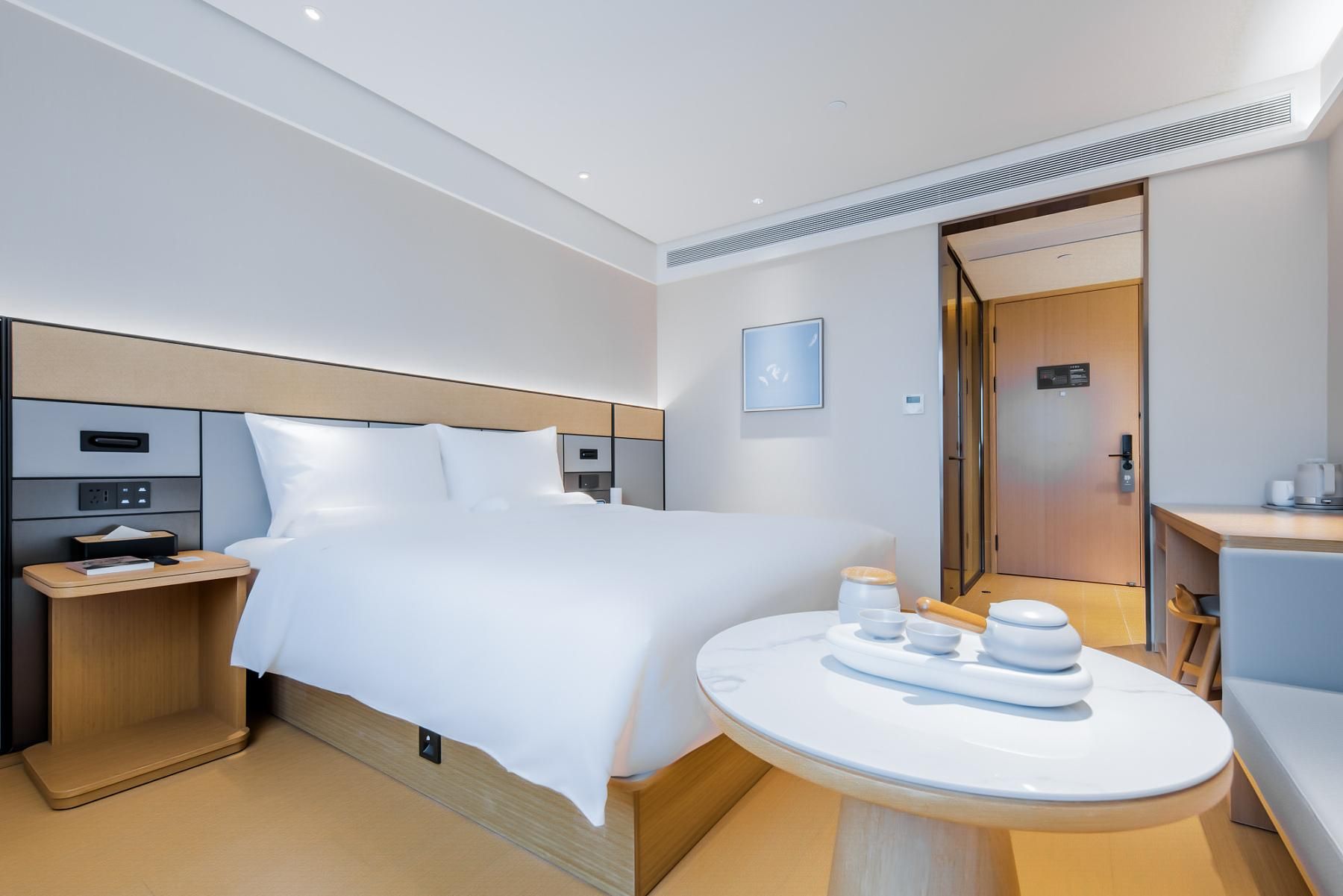 Et moderne hotelværelse med en stor seng, sengeborde, et rundt bord med tesæt og en dør til et badeværelse.