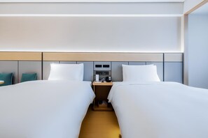 A hotel room with two beds, a bedside table with a lamp, a small table with a phone and a clock, and a wall-mounted control panel. - Ji Hotel (Hefei)