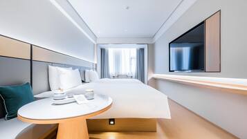 A modern hotel room with a bed, bedside table, TV, and a view of the hallway.