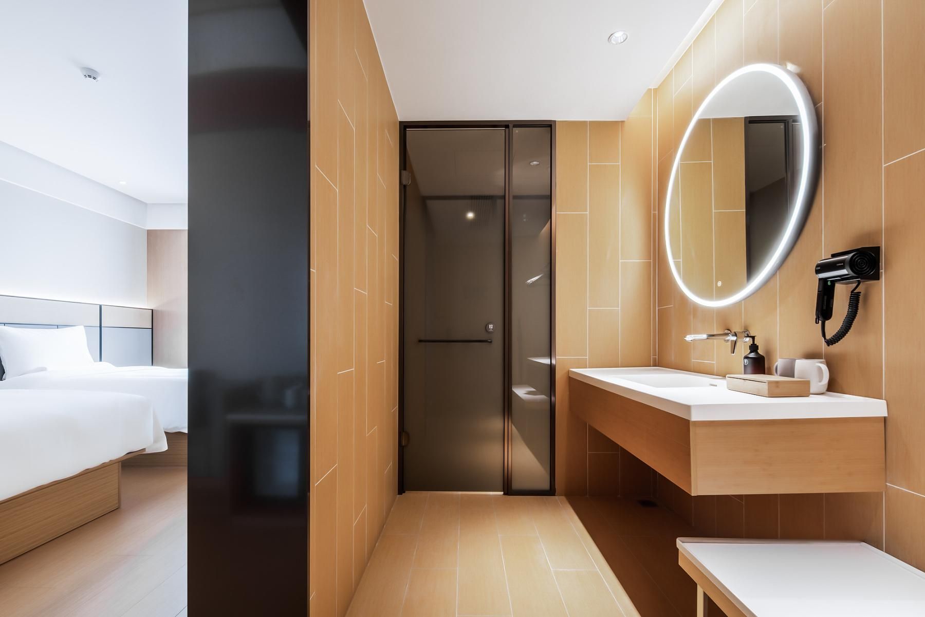 A modern hotel room with a bed, a bathroom with a mirror, and a shower.