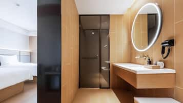 A modern hotel room with a bed, a bathroom with a mirror, and a shower.