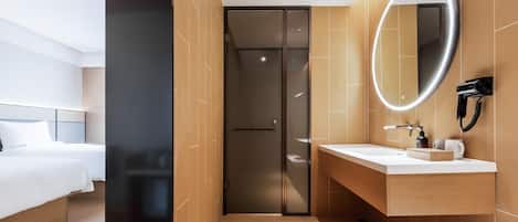 A modern hotel room with a bed, a bathroom with a mirror, and a shower.