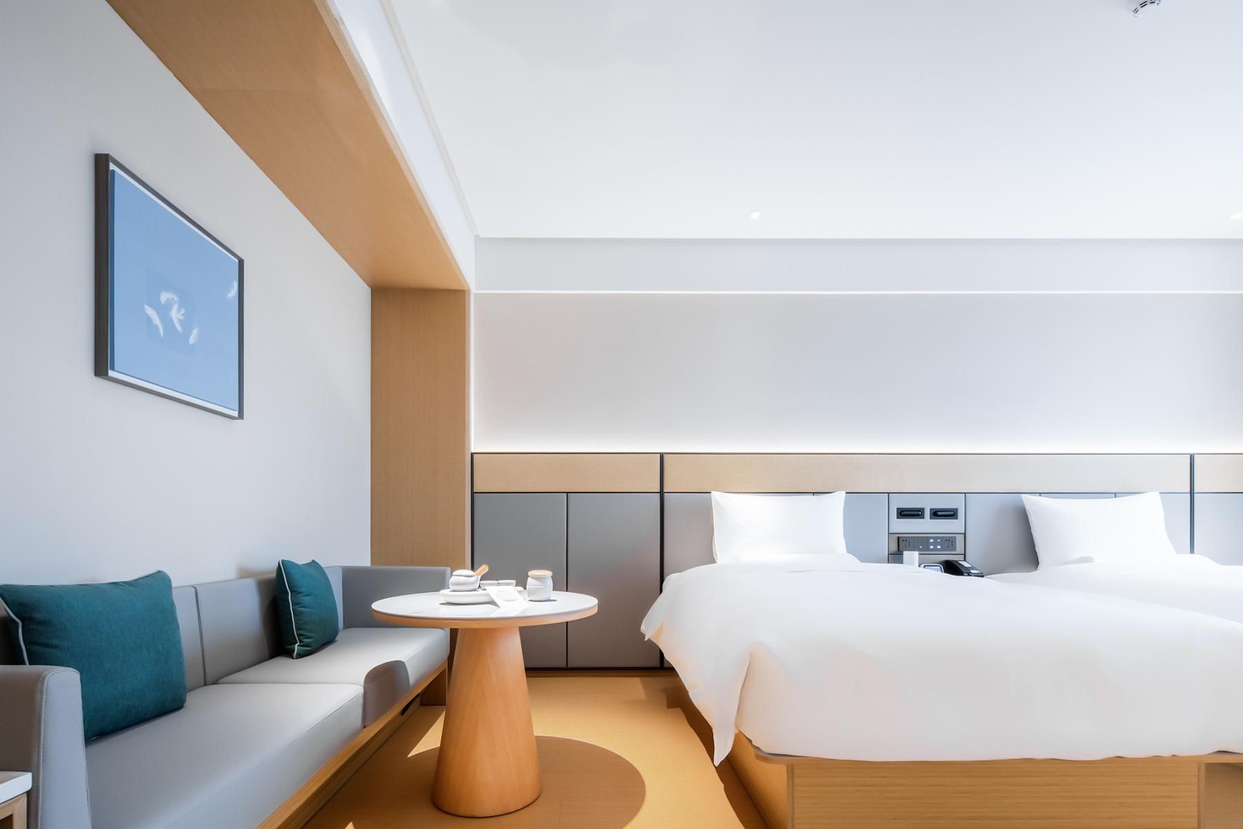 Habitació d'hotel moderna amb llit, sofà, taula rodona i televisió penjada a la paret.
