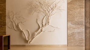 A wall with a tree-like sculpture, marble walls, and a wooden bench. - Emara Ole Sereni (Syokimau)