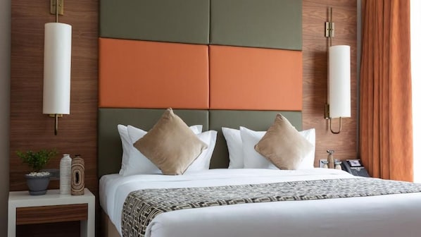 A hotel room with a bed, two bedside tables, a potted plant, and a wall-mounted lamp. - Emara Ole Sereni (Syokimau)