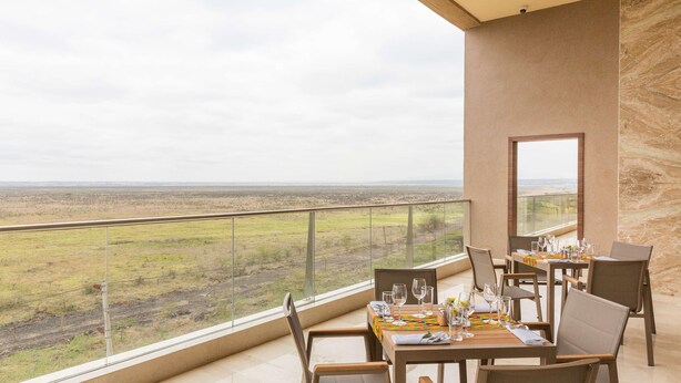 A dining area with tables set for two, overlooking a savannah landscape. - Emara Ole Sereni (Syokimau)
