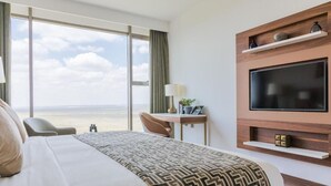 A hotel room with a large bed, a desk, a TV mounted on the wall, and a view of the ocean. - Emara Ole Sereni (Syokimau)