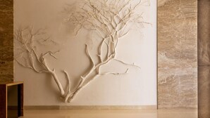 A wall with a tree-like sculpture, marble walls, and a wooden bench. - Emara Ole Sereni (Syokimau)