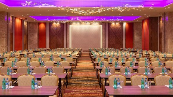 A conference room with rows of tables and chairs, a carpeted floor, and a stage at the front.