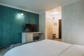 A bedroom with a bed, a television on a wooden cabinet, and a door leading to another room. - Suru Hotel (Busteni)
