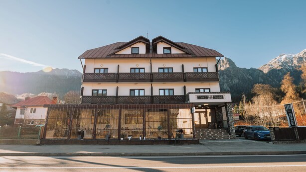 Um hotel de vários andares com fachada simétrica, janelas amplas e montanhas ao fundo.