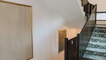 Un escalier recouvert d’une moquette à motifs, une main courante en bois foncé et un mur orné d’un grand tableau encadré.
