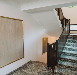 A staircase with patterned carpet, a dark wooden handrail, and a wall with a large framed artwork. - Suru Hotel (Busteni)
