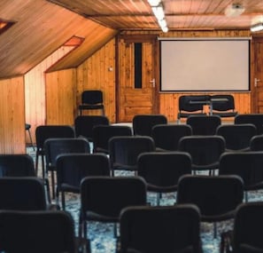 Une salle de conférence dotée d’un grand écran, de murs en bois et de rangées de chaises.