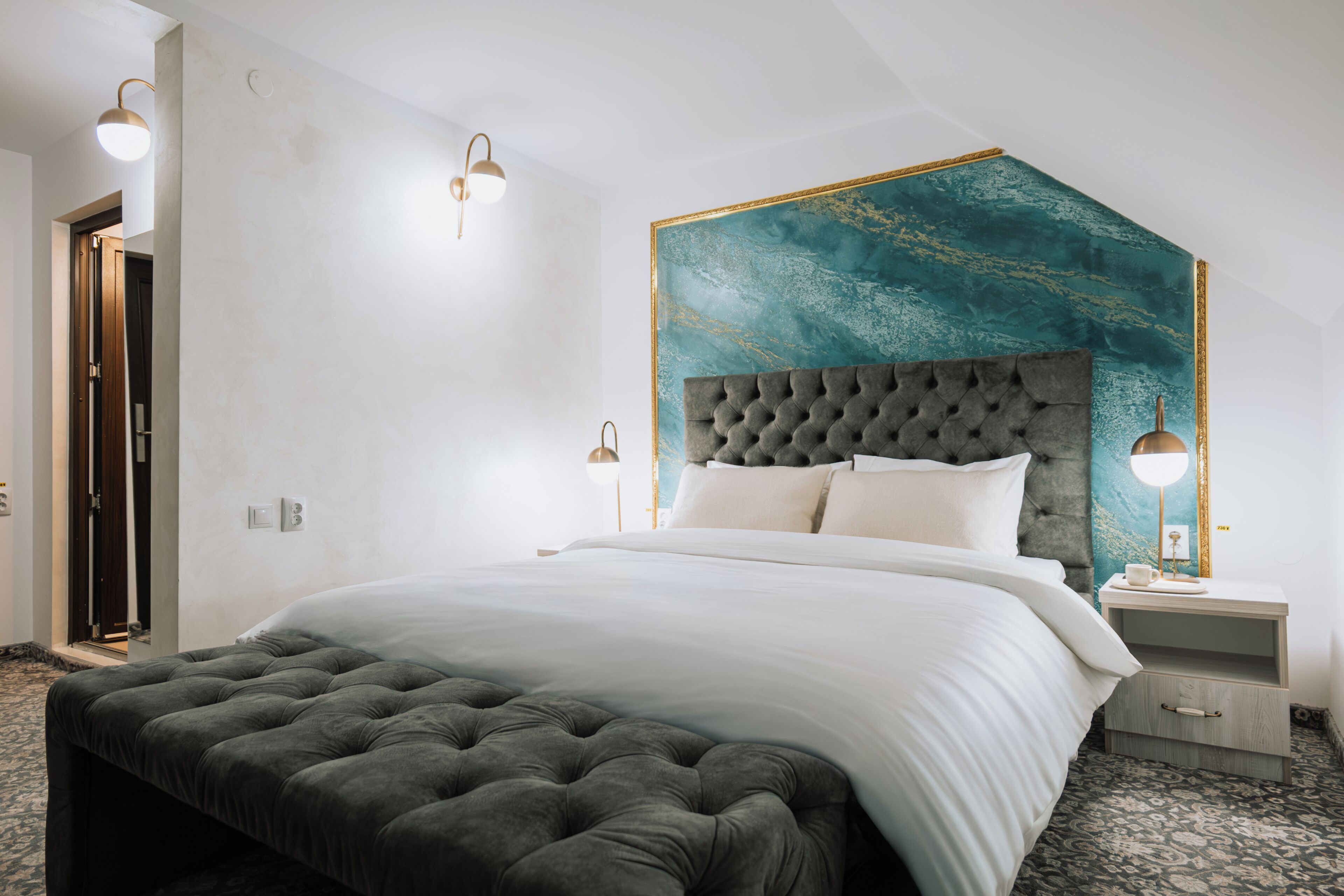 Un dormitorio con cabecera capitonada, una cama grande, mesitas de noche y un aplique de pared.