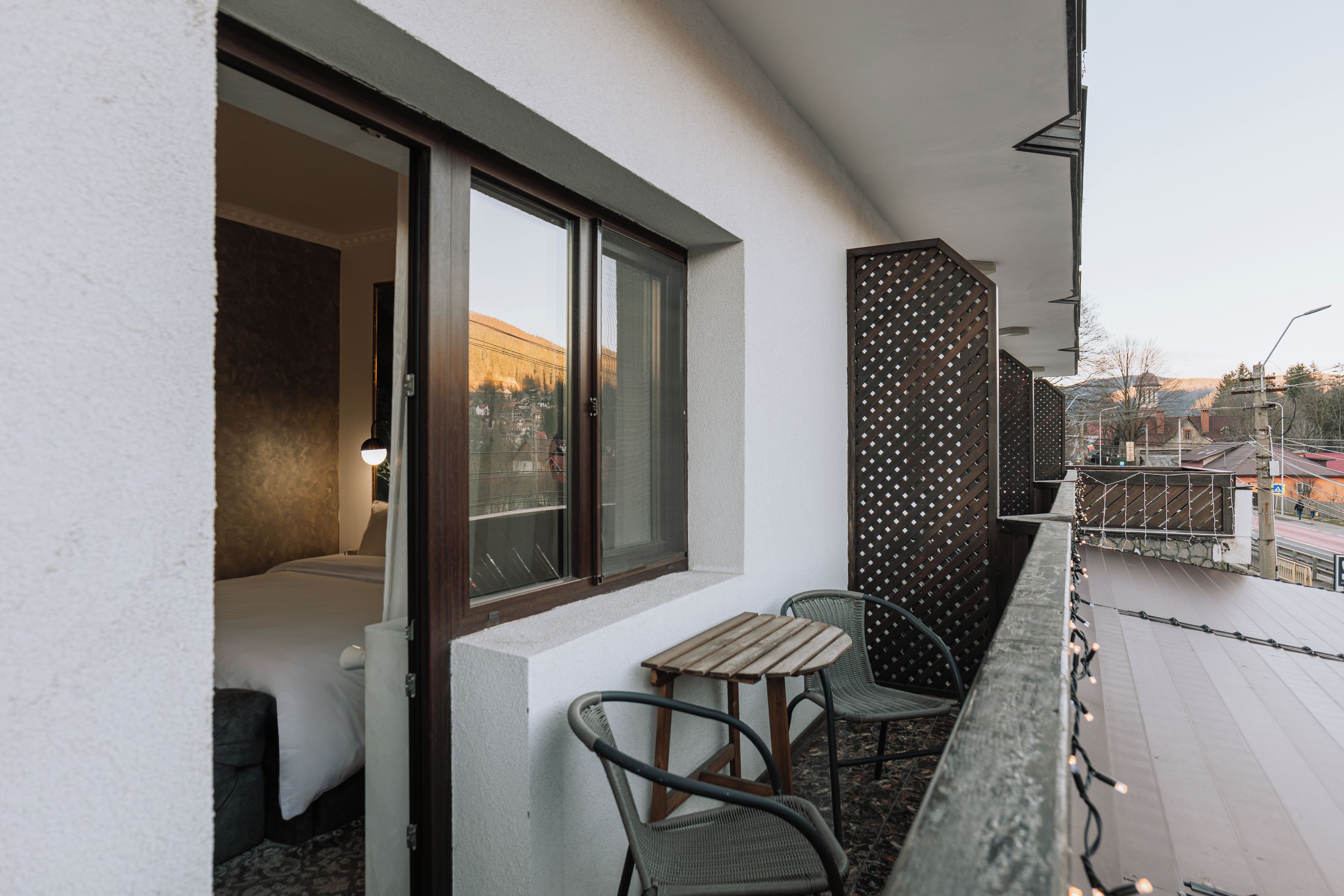 Un balcon avec une table et des chaises, une fenêtre donnant sur des immeubles et une clôture décorative.