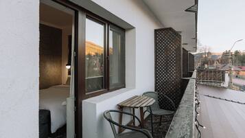Un balcon avec une table et des chaises, une fenêtre donnant sur des immeubles et une clôture décorative.