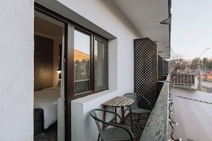 Un balcon avec une table et des chaises, une fenêtre donnant sur des immeubles et une clôture décorative.