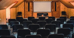 A conference room with a large screen, rows of chairs, and wooden walls. - Suru Hotel (Busteni)