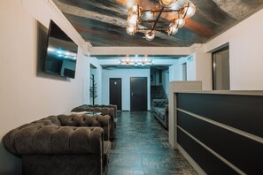 A hallway with a dark wooden floor, a tufted sofa, a television on the wall, and a chandelier. - Suru Hotel (Busteni)