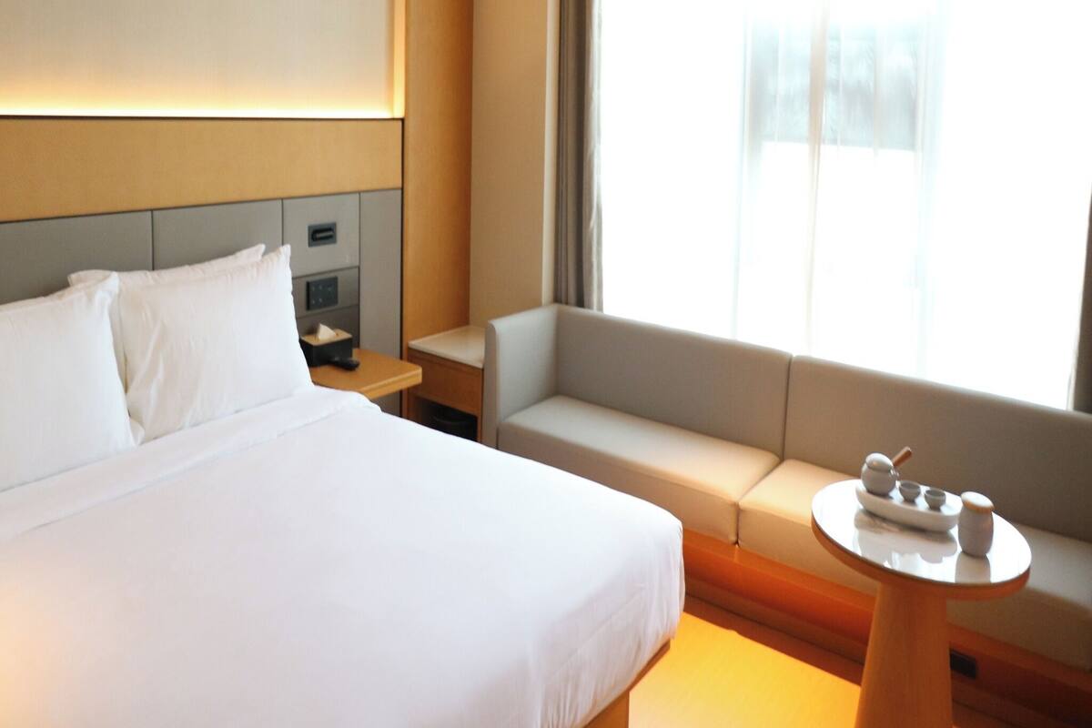 A hotel room with a bed, a sofa, a small table, and a window with curtains.