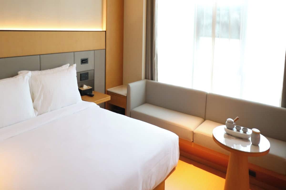 A hotel room with a bed, a sofa, a small table, and a window with curtains.