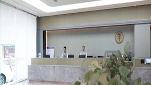 Un mostrador de recepción con dos empleados, un cartel con caracteres chinos y una puerta de vidrio.