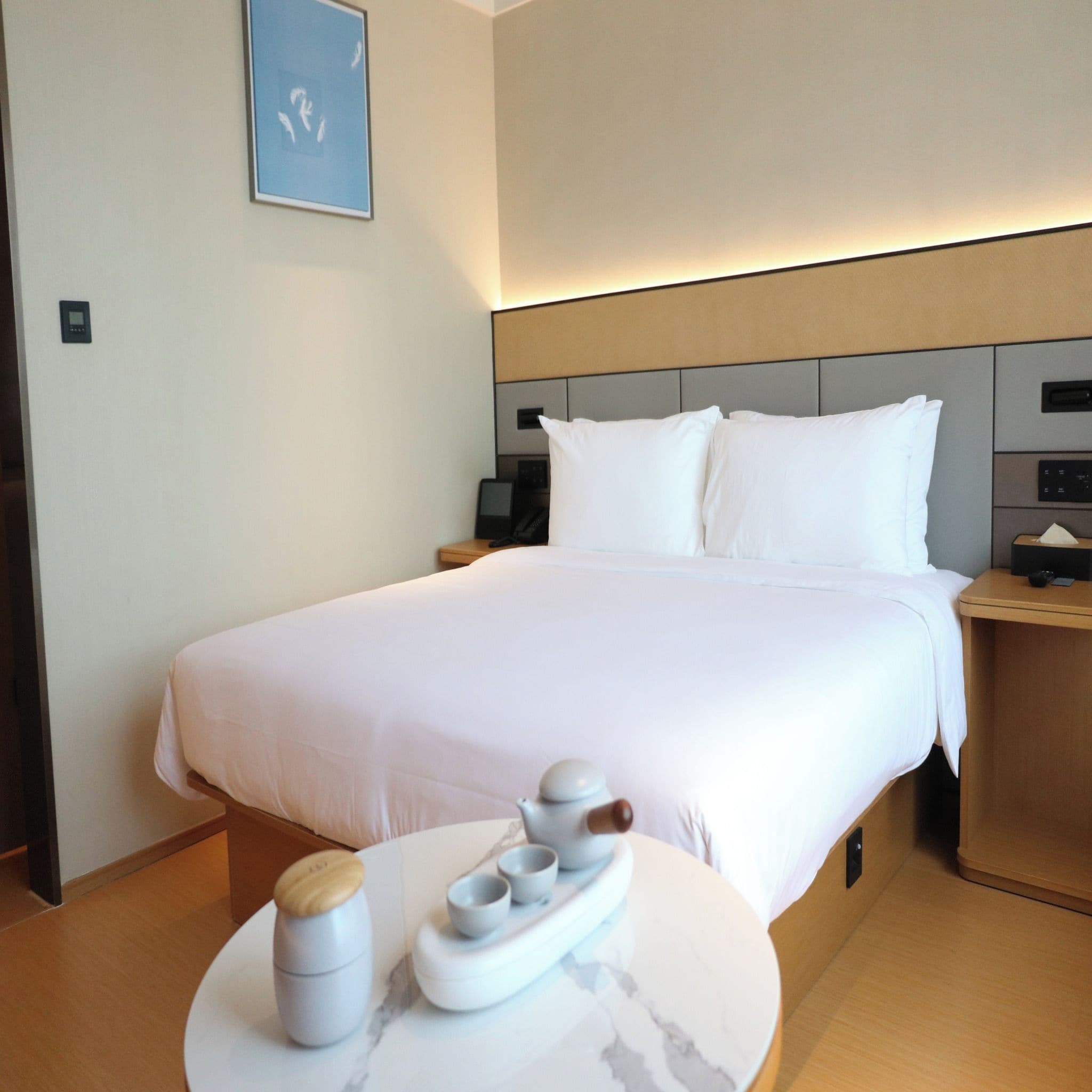 A hotel room with a large bed, bedside tables, a round table with a water dispenser, and a wall-mounted phone.