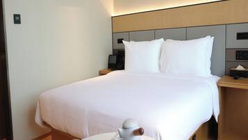 A hotel room with a large bed, bedside tables, a round table with a water dispenser, and a wall-mounted phone.