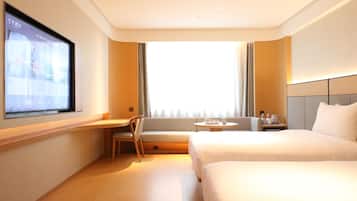 A hotel room with a bed, a desk, a chair, a TV, and a window.