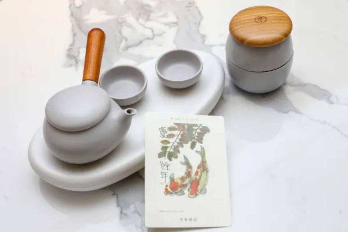 A set of white ceramic tea utensils, including a teapot, cups, and a small container, on a marble surface.