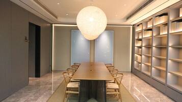 A conference room with a long table, chairs, a central hanging light fixture, and bookshelves along the walls.