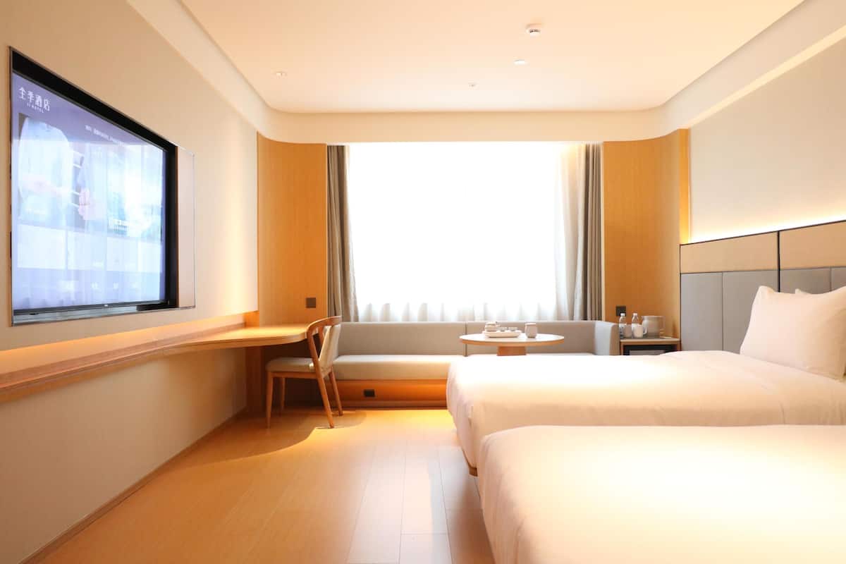 A hotel room with a bed, a desk, a chair, a TV, and a window.