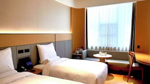 Habitación de hotel con dos camas, una mesita, un sofá y una ventana con cortinas.