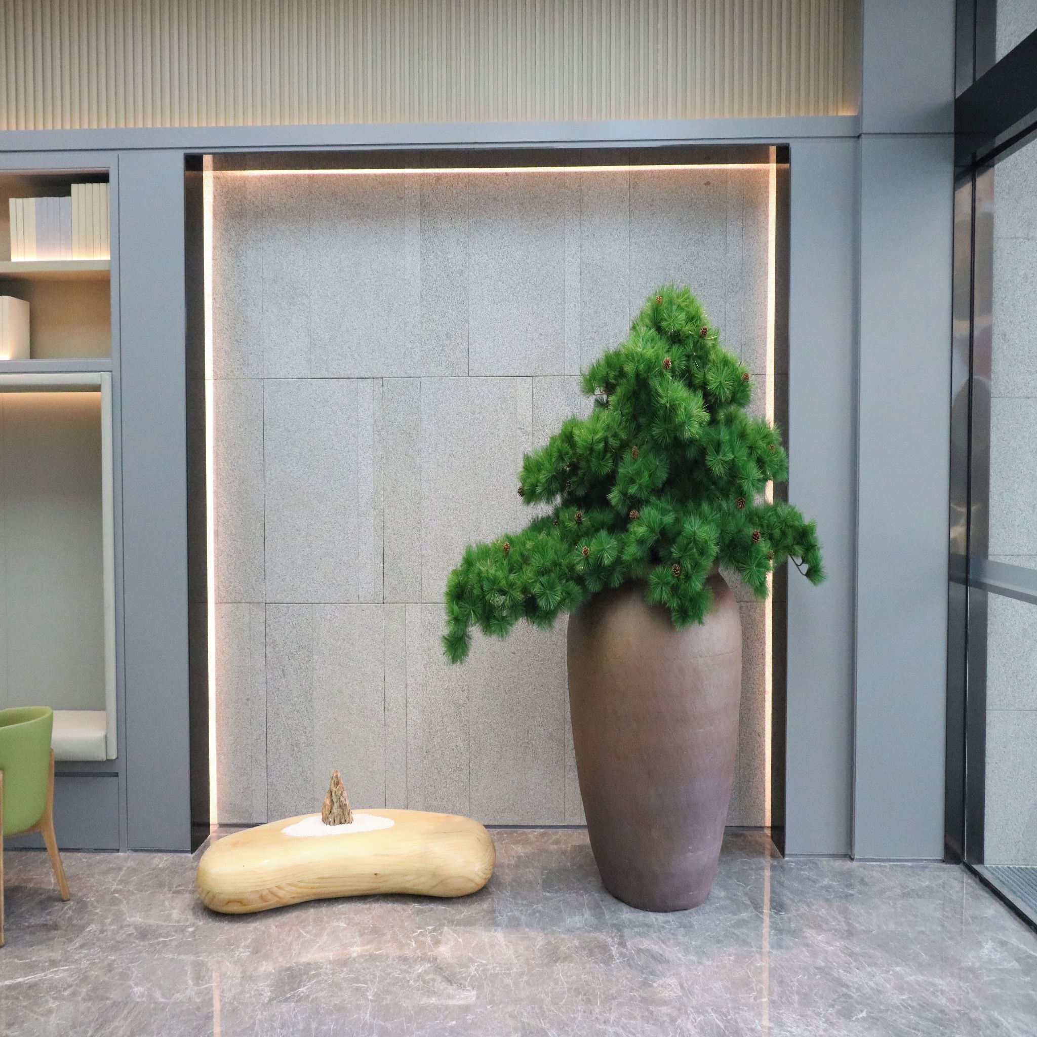 A modern lobby with a large potted plant, a unique wooden sculpture, and a sleek reception desk.
