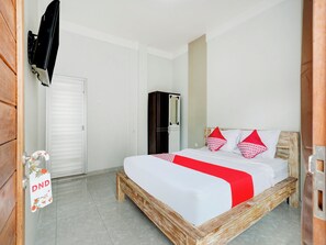 Una camera da letto con un letto in legno, biancheria da letto bianca e cuscini rossi. Si nota un armadio e un televisore montato a parete.