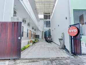 Un bâtiment doté d’une passerelle couverte, d’une entrée sécurisée par un portail et d’une enseigne indiquant « OYO Melasti Hills Room & Cafe ».