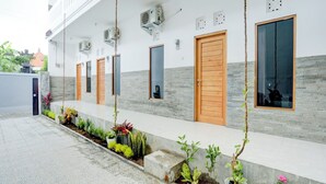 A building with a series of doors and windows, air conditioning units, and a tiled walkway with potted plants. - OYO 90756 Melasti Hills Room & Cafe (Ungasan)