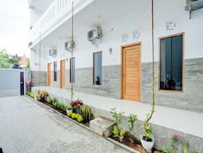 Un bâtiment doté d’une série de portes et de fenêtres, de climatiseurs et d’un trottoir carrelé agrémenté de plantes en pot.