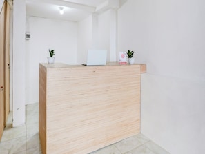 A wooden reception desk with a laptop and two potted plants. - OYO 90756 Melasti Hills Room & Cafe (Ungasan)