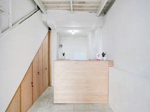 A reception desk in a hallway with a wooden staircase on the left and a white wall with a ceiling light. - OYO 90756 Melasti Hills Room & Cafe (Ungasan)
