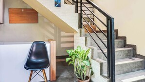 Una escalera con barandilla negra, pared de ladrillo blanco y una planta en maceta.