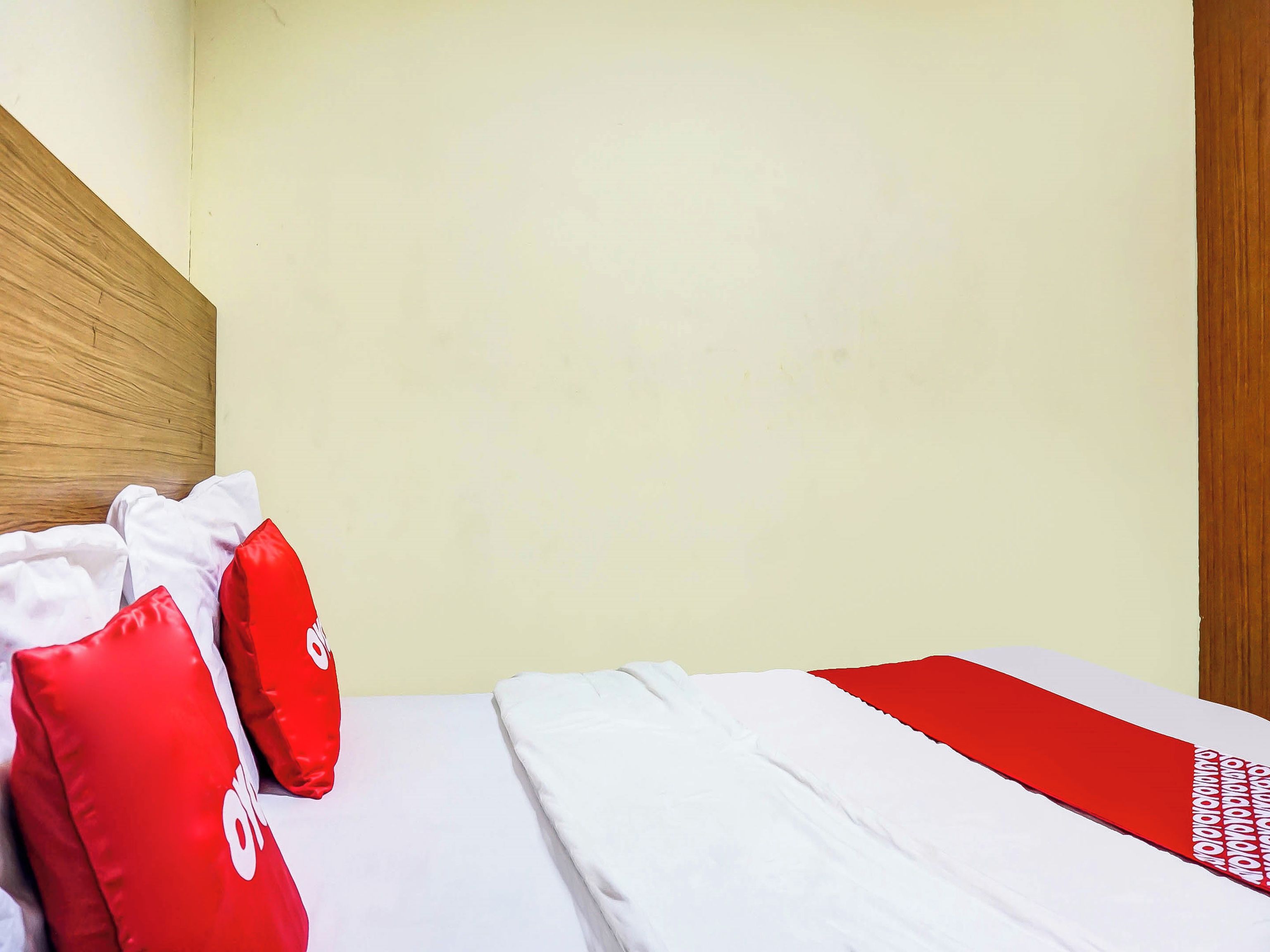 A hotel room with a wooden headboard, a bed with white and red bedding, and a plain wall.