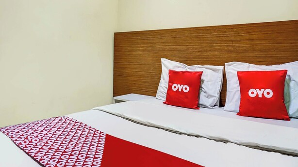 Una cama con cabecera de madera, dos almohadas rojas con el texto 'OYO' y una colcha estampada.