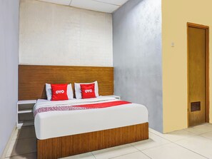 Una habitación de hotel con cama, cabecera de madera, colcha roja y blanca, y pared con diseño de ladrillos blancos.