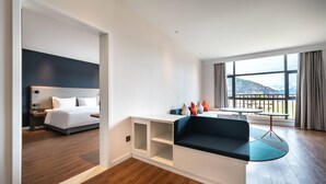 A modern hotel room with a bed, a seating area with a table, and a view of the mountains.