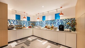 A modern kitchen with white cabinets, blue and white checkered backsplash, and orange pendant lights.
