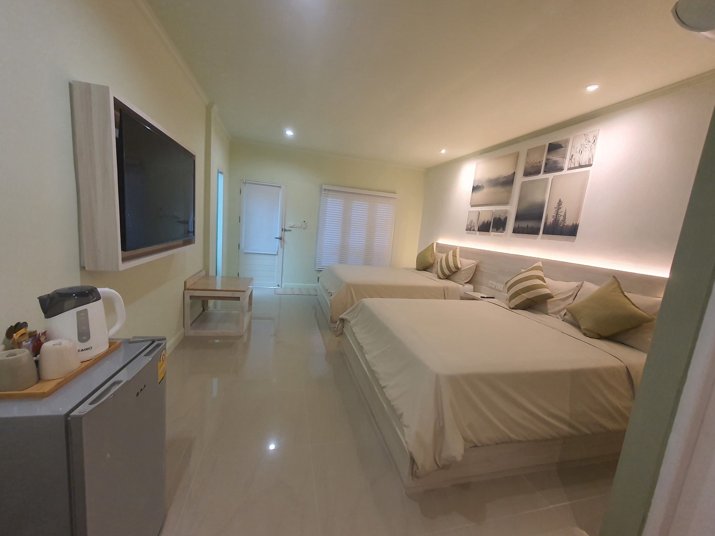 A hotel room with two beds, a TV, a kitchenette, and a bathroom.