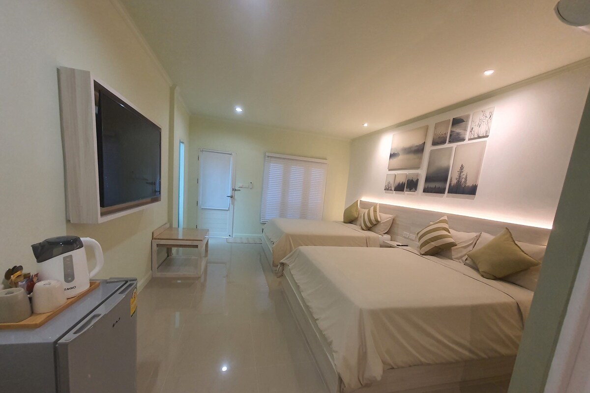 A hotel room with two beds, a TV, a kitchenette, and a bathroom.